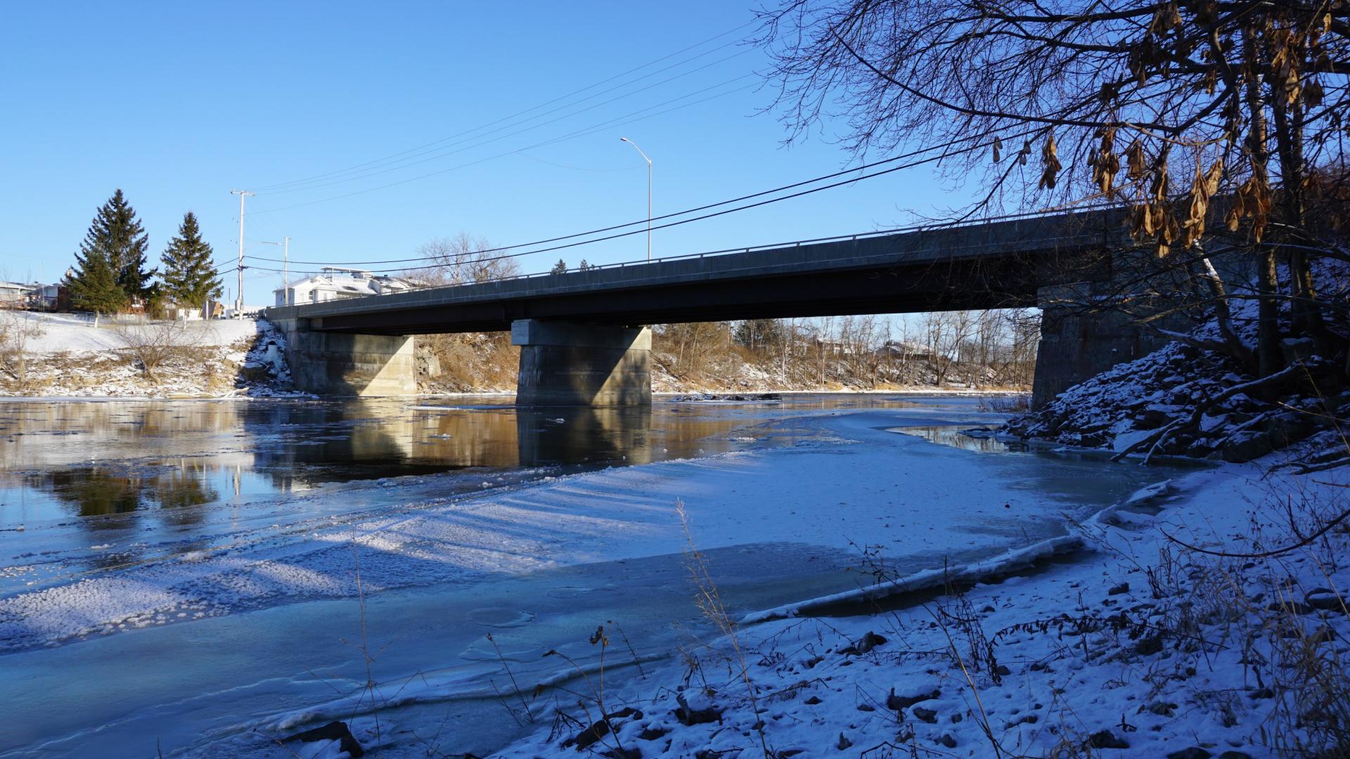 Frozen river under a bridge on a clear, sunny winter day.