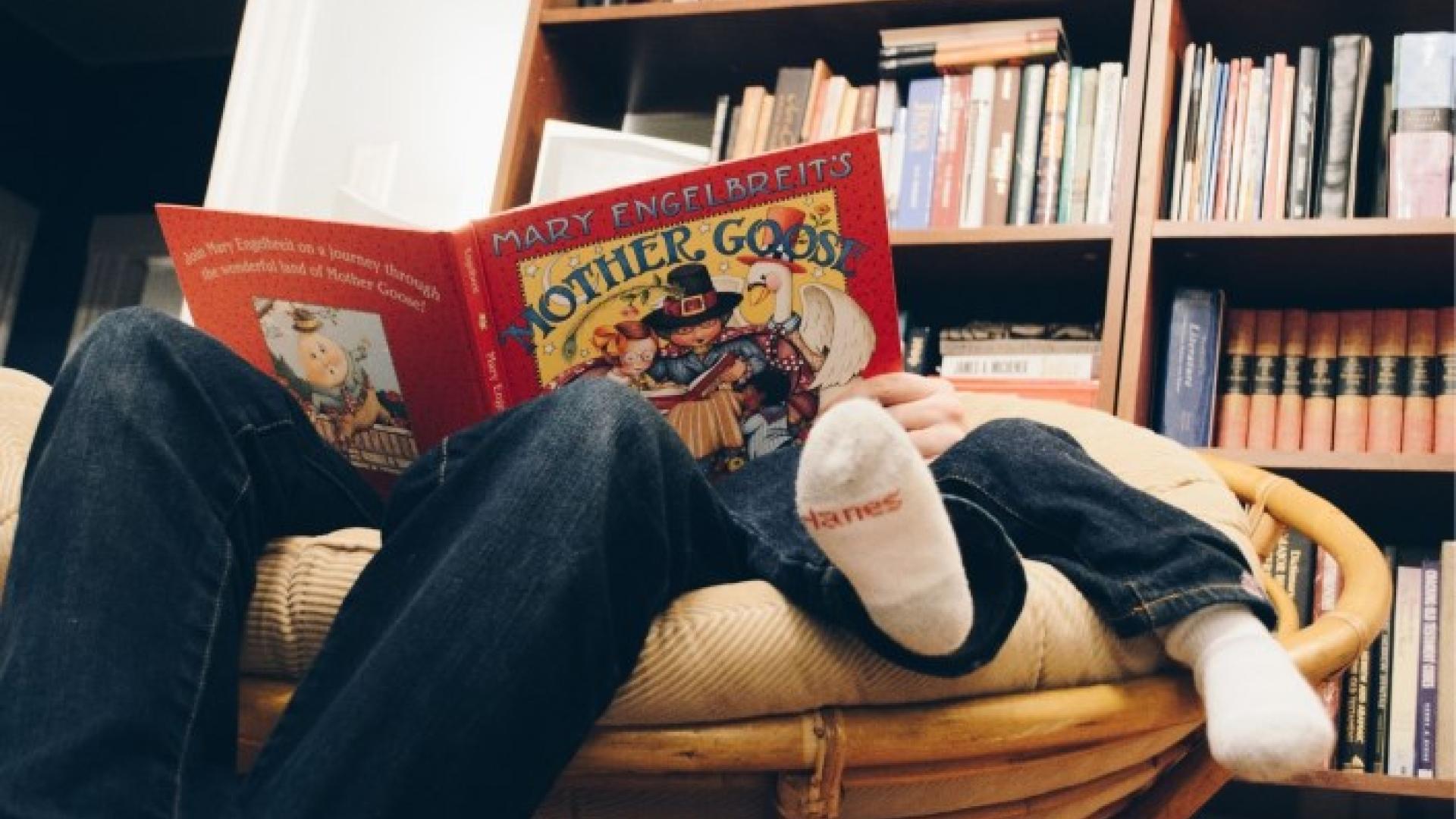 Child reading a colorful book in a cozy chair, surrounded by bookshelves.