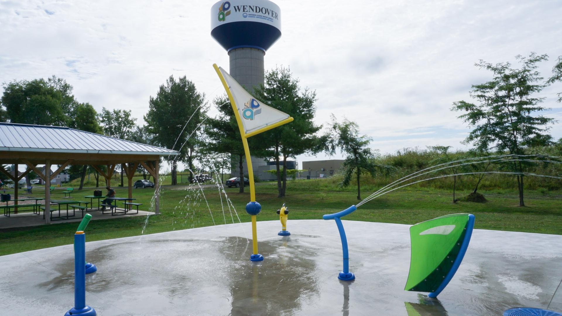 Water spray park with colorful fountains and water tower in background.