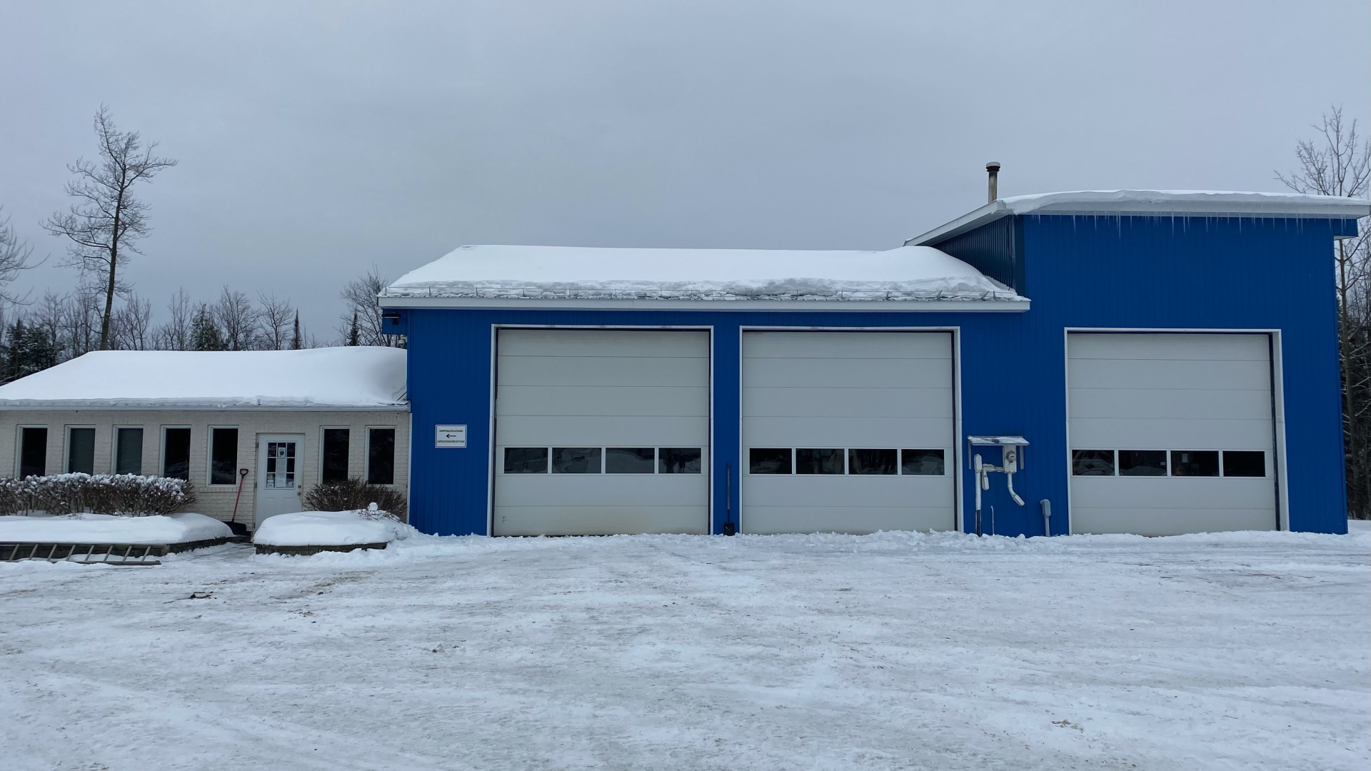 Blue building with three garage doors, surrounded by snow.
