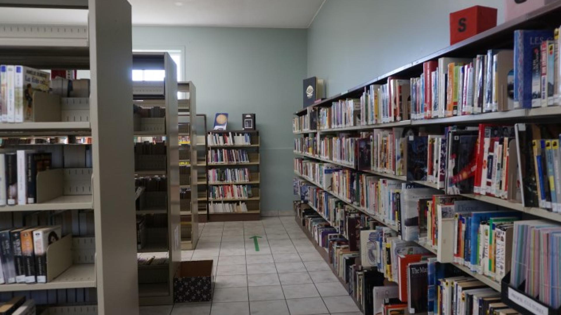 Library aisle with books on shelves, tile flooring, and green arrows on the floor.