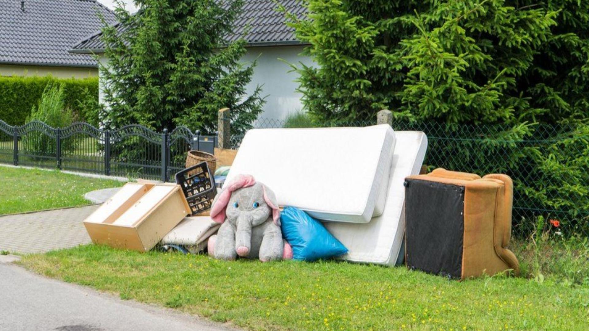 Old furniture and a stuffed toy elephant on a roadside lawn.
