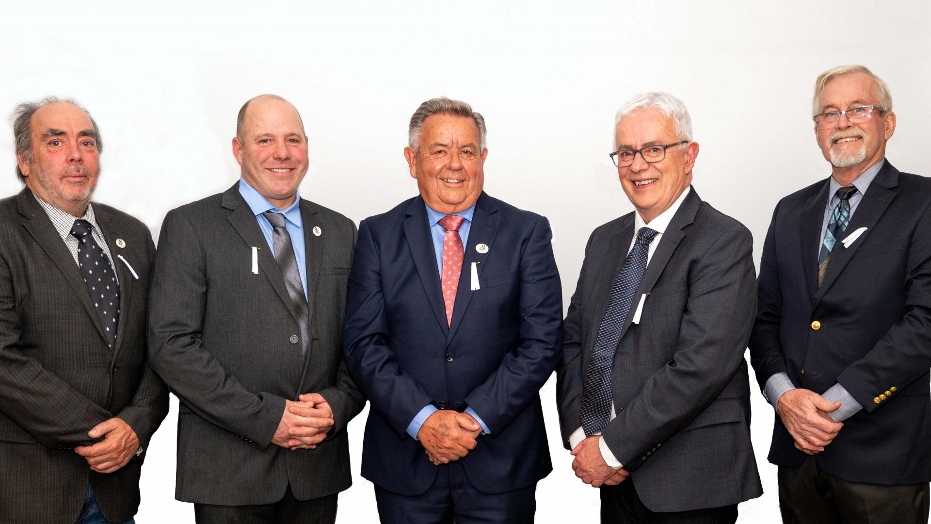 Five men in suits smiling, standing in a row against a white background.