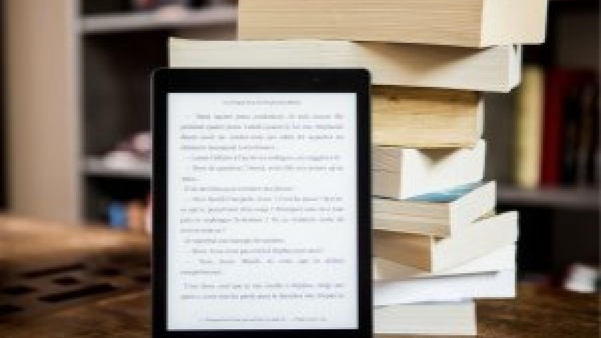E-reader displaying text, leaning against stacked books on a table.