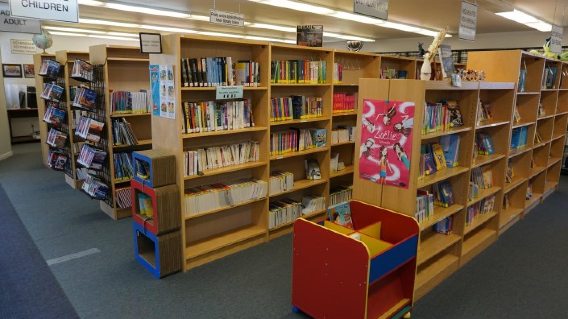 Bookshelves in a library with colorful book cart in the foreground.