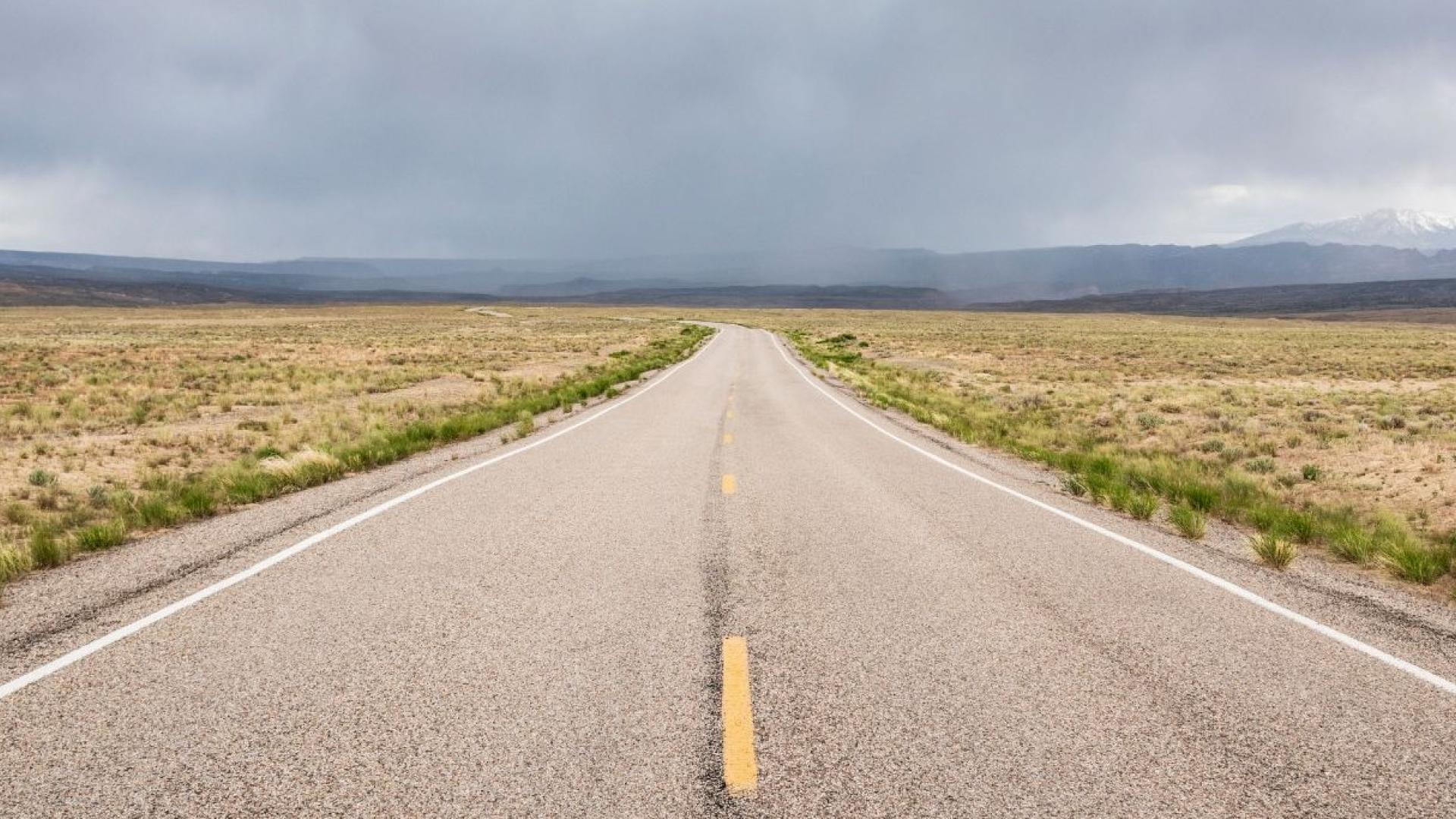 Empty road stretching into cloudy horizon over barren landscape.