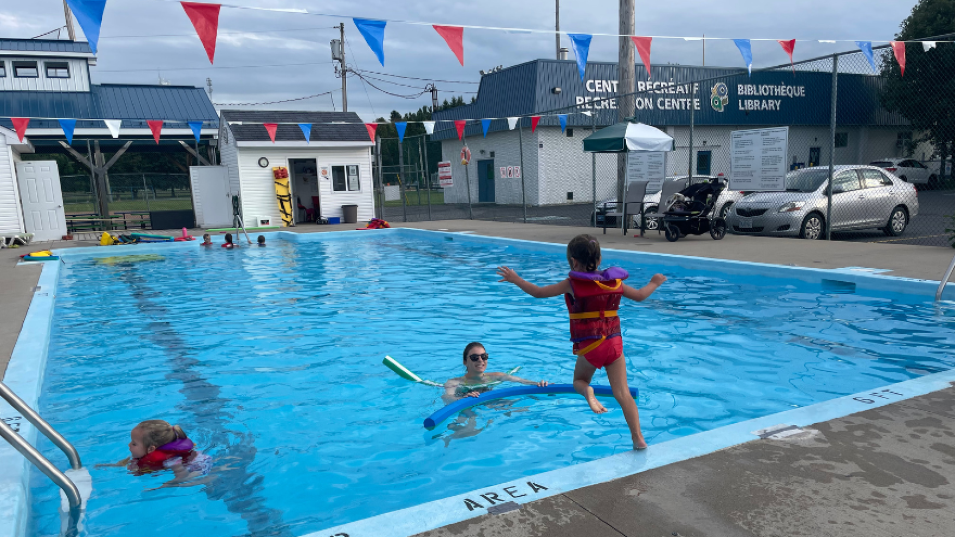 Petite fille saute dans la piscine sous la surveillance d'une jeune femme