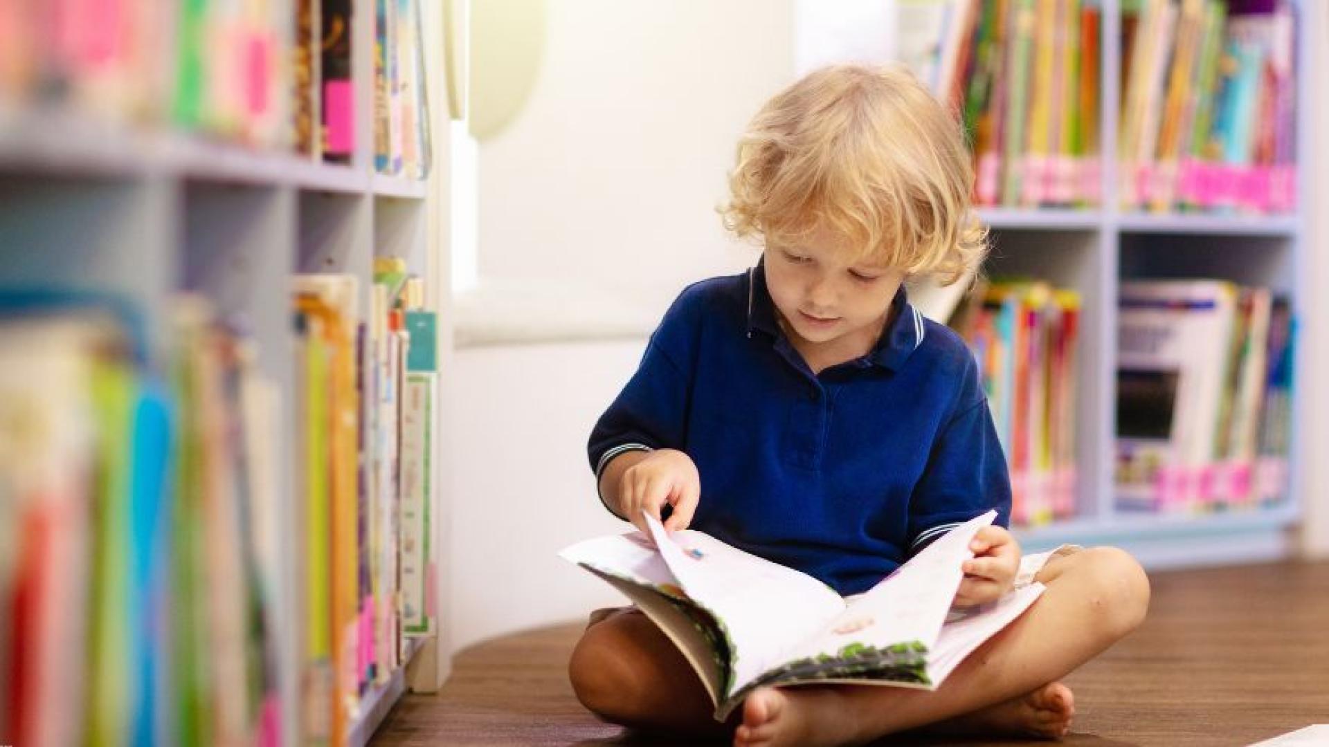 Child reading a book sitting on a library floor