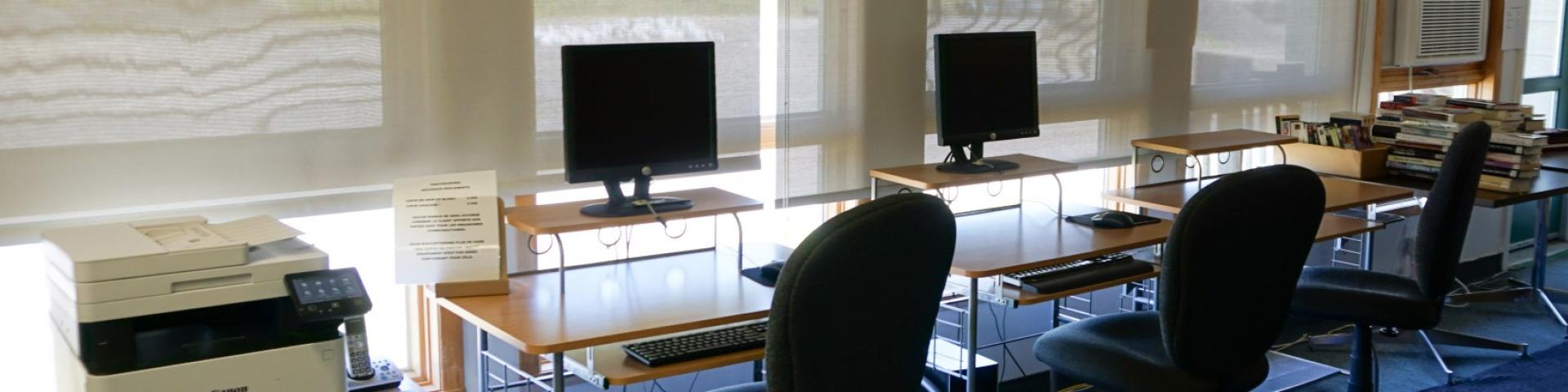 Computer workstations with chairs in a sunlit room.