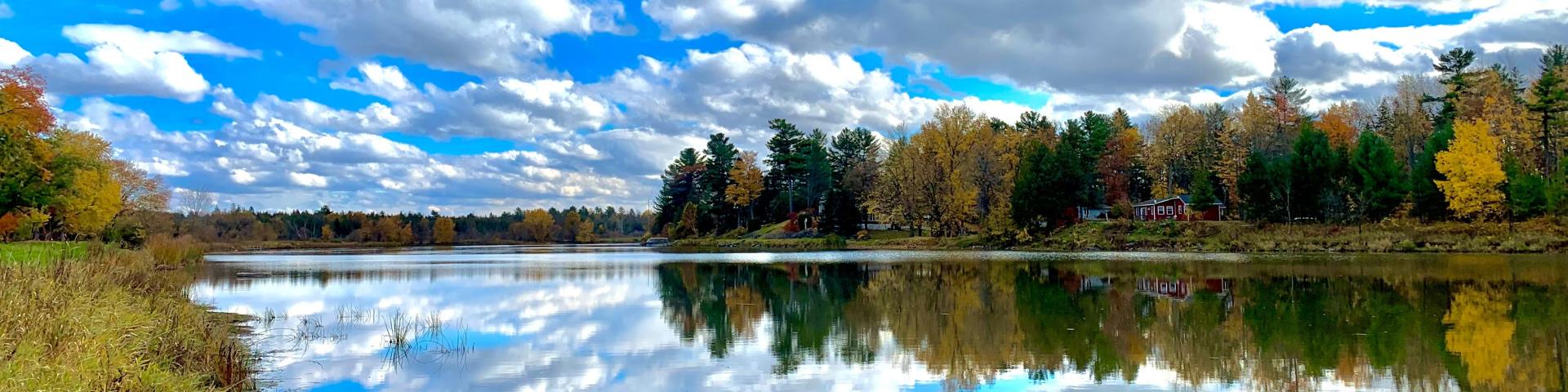 Calm lake with autumn trees and clouds reflected on the water.