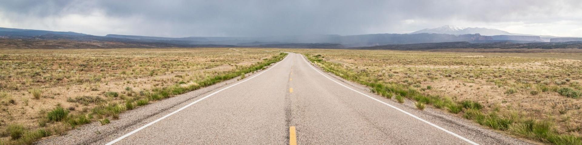 Empty road stretching into cloudy horizon over barren landscape.