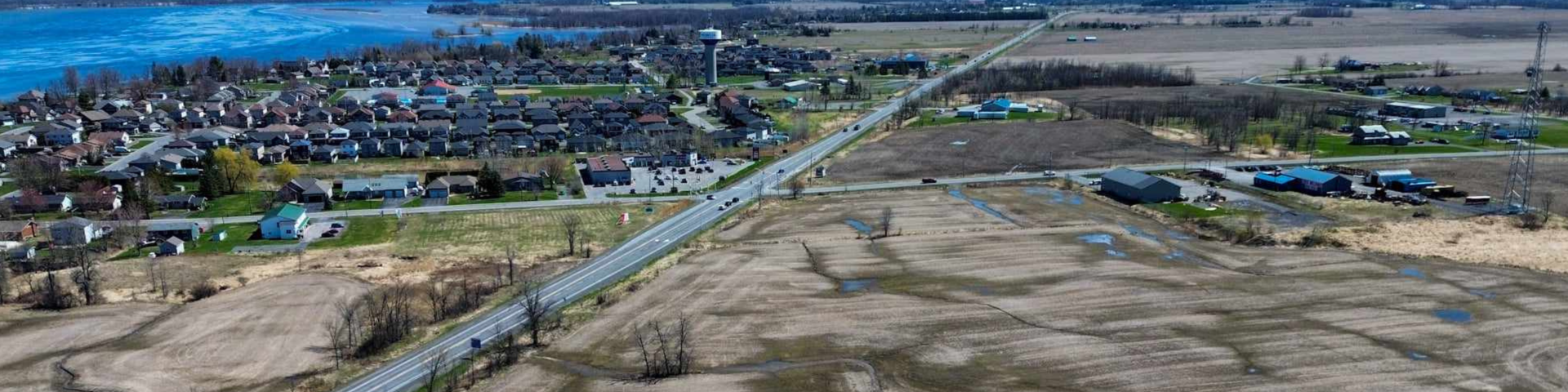 Aerial view of a road dividing a residential area and open fields, with a river on the left.