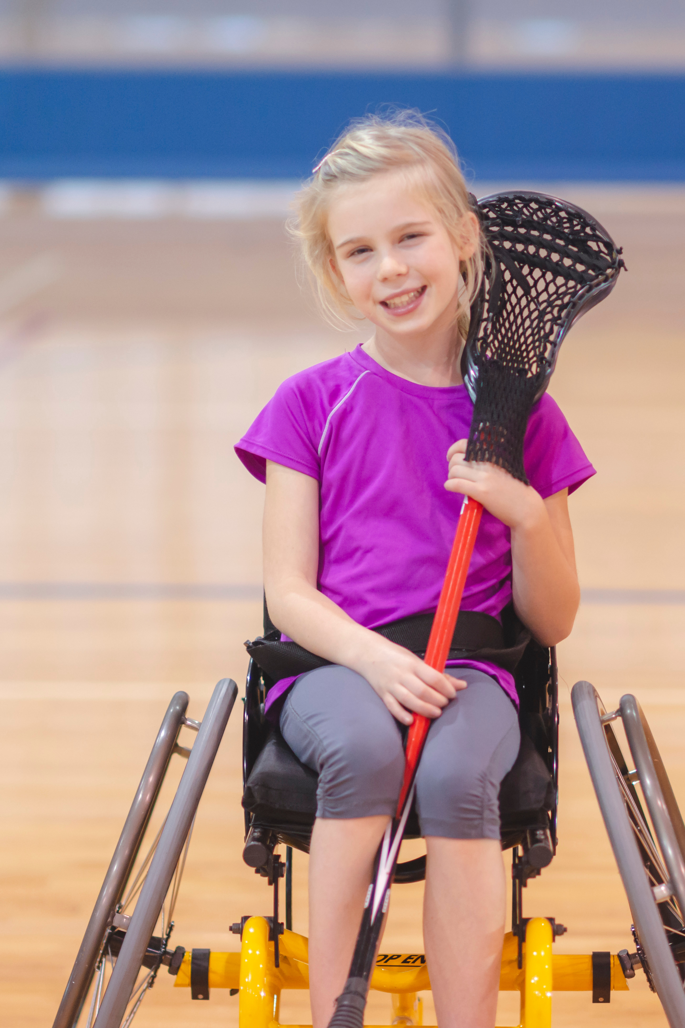 A little girl holding a lacrosse stick and smiling at the camera