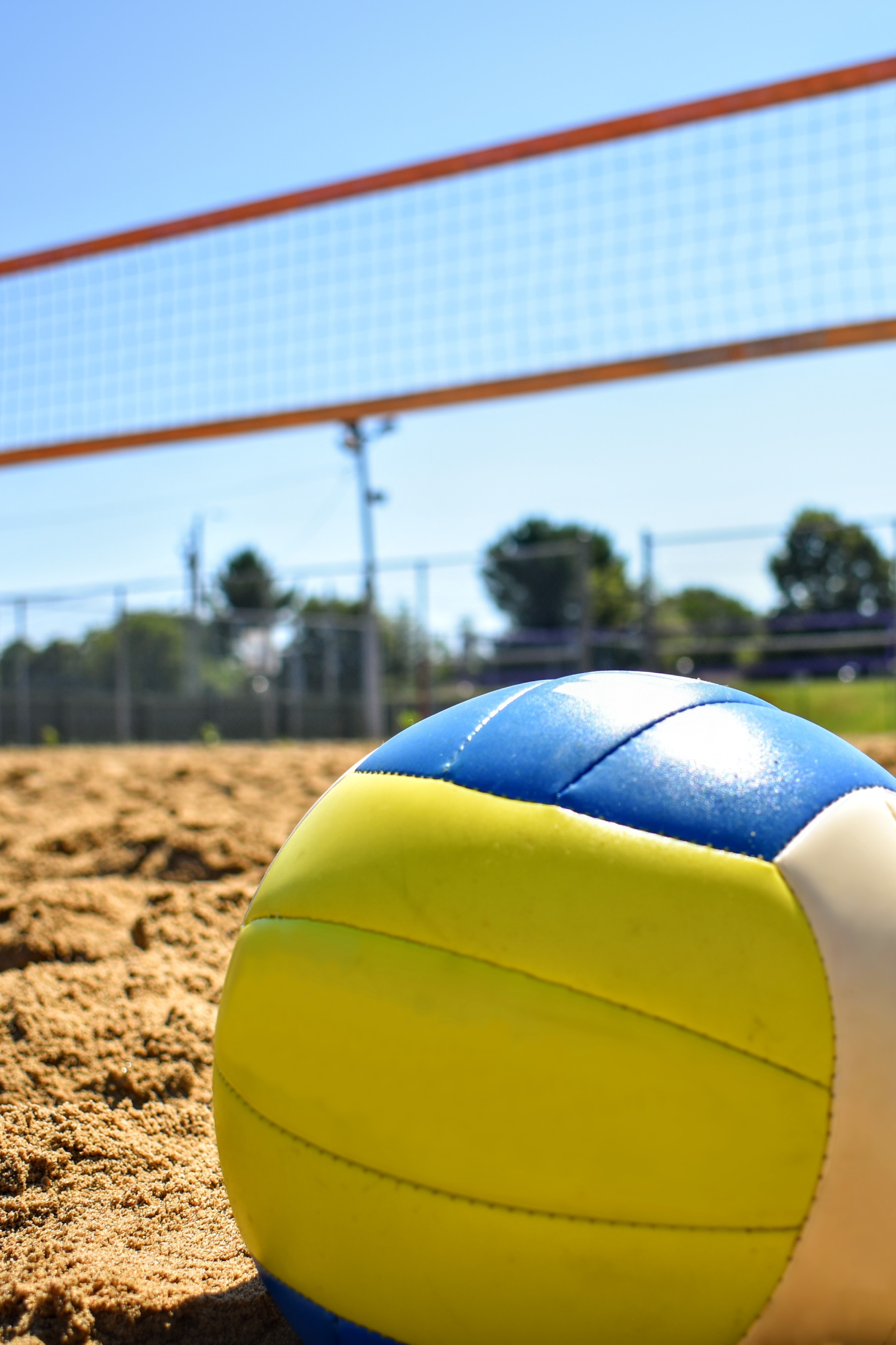 a volleyball on the sand with the net in background.