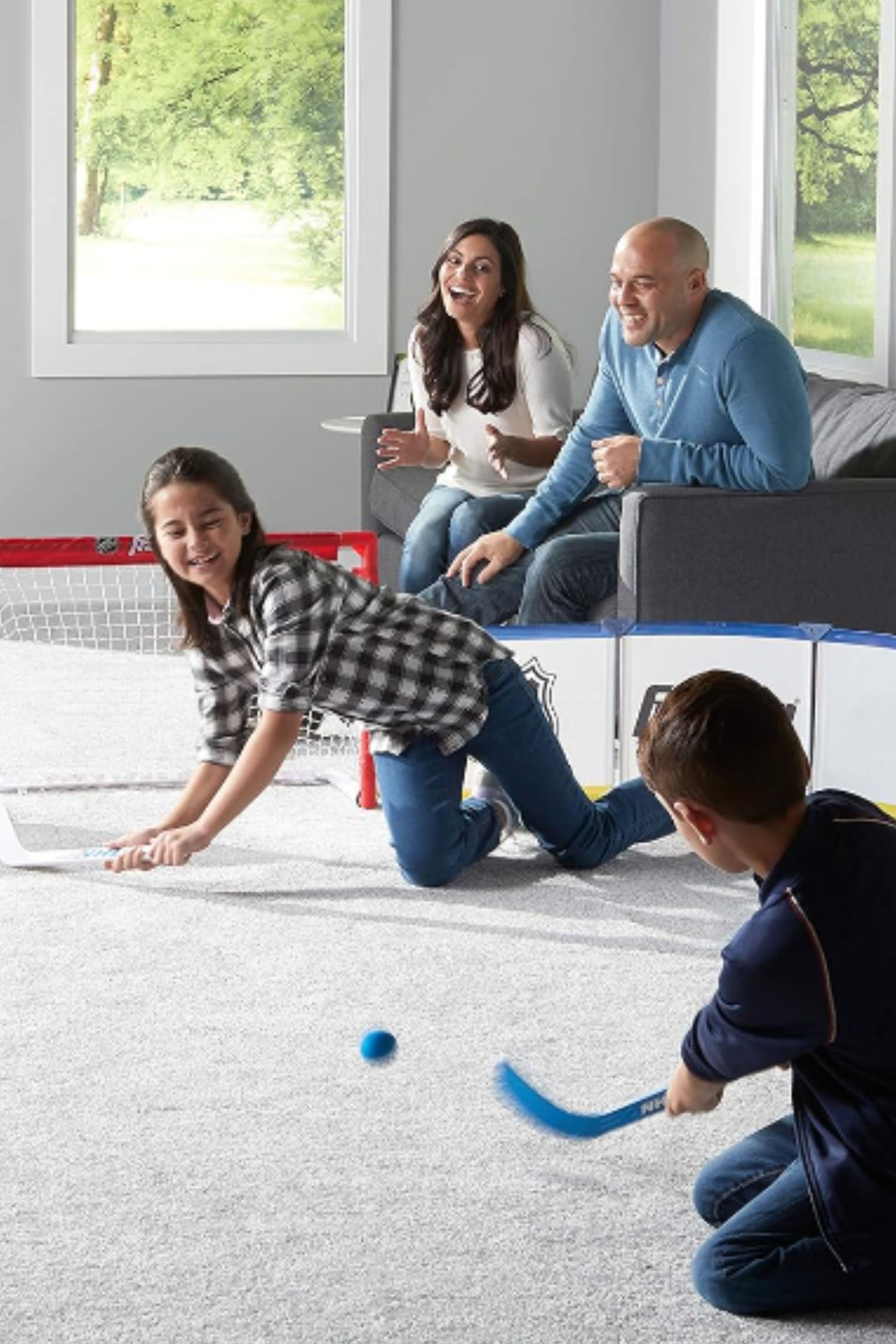A girl and a boy playing mini sticks in their living room with parents watching them. 