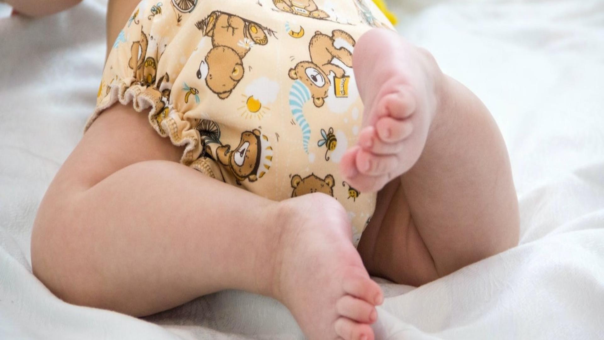 Baby wearing a teddy bear print diaper, lying on a white blanket.
