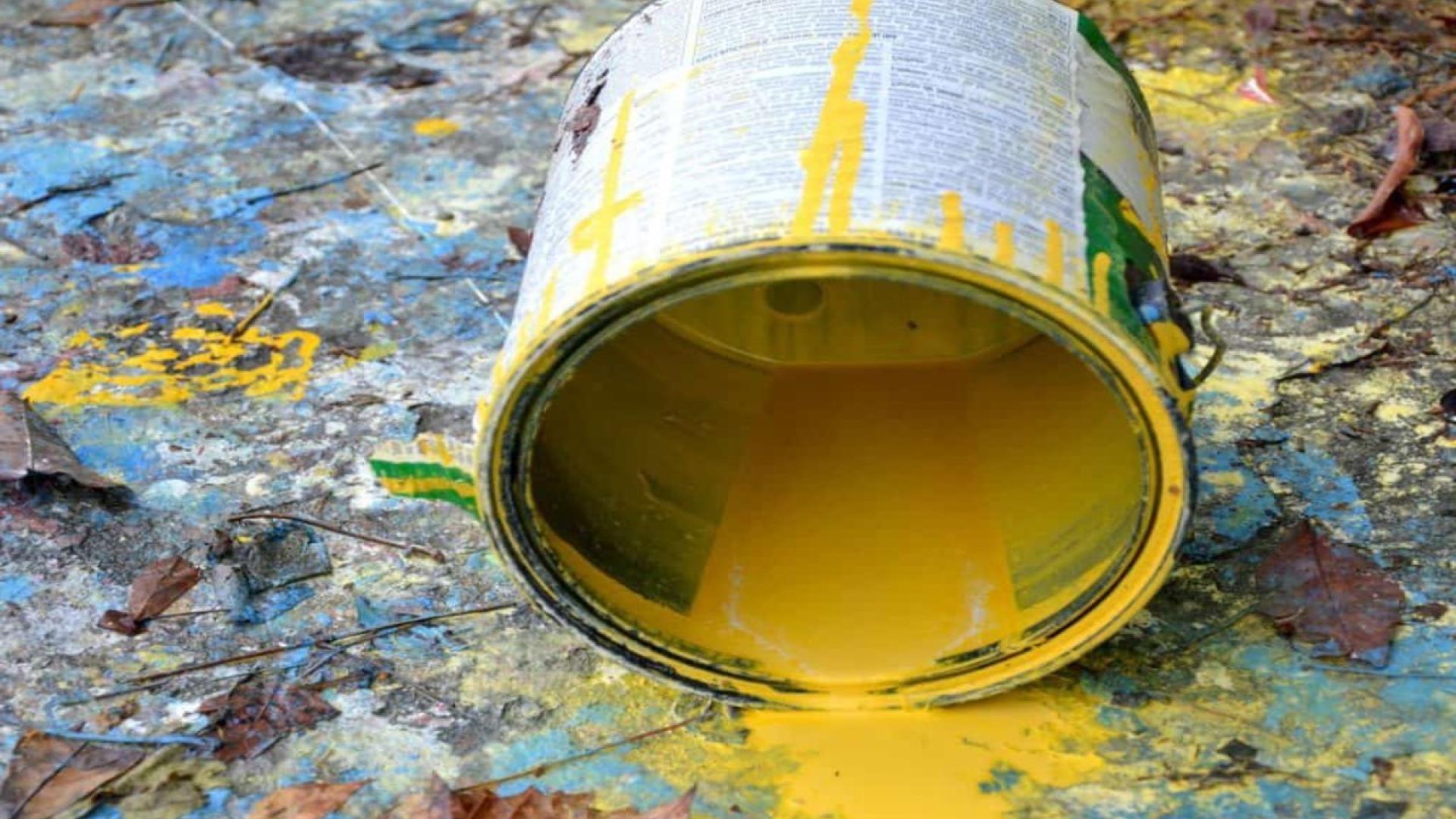 Yellow paint spilled from a can onto a colorful, textured floor.