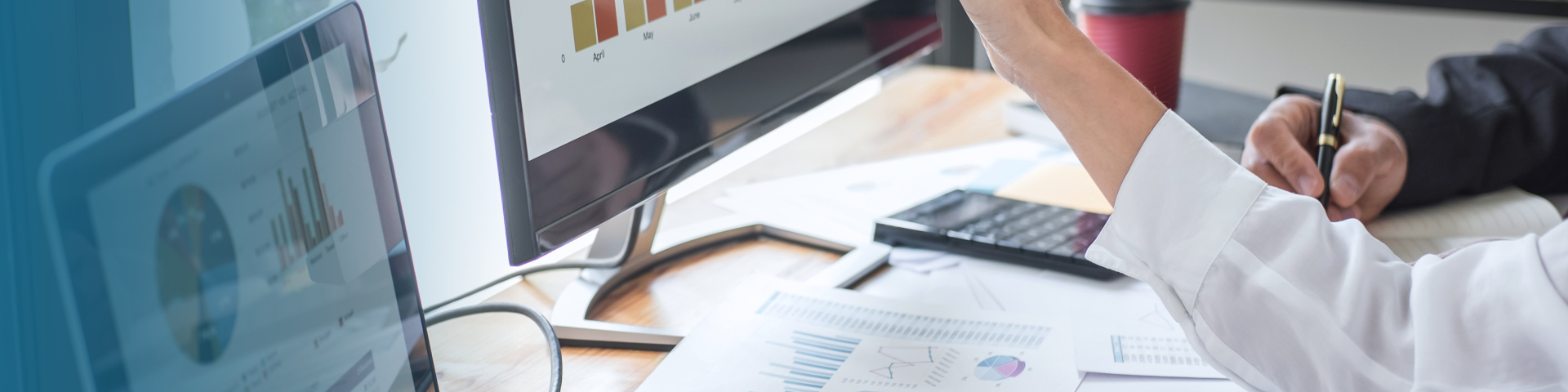 Graphs and charts on dual monitors, two people in discussion.